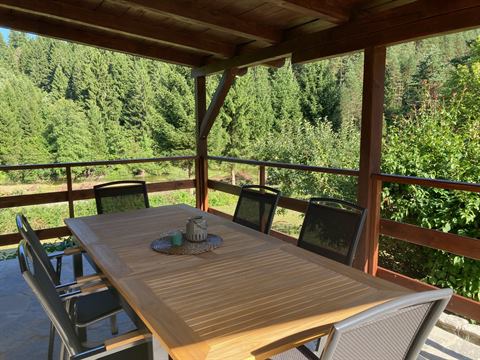 Überdachte Holzterrasse mit Esstisch und Blick auf den Wald