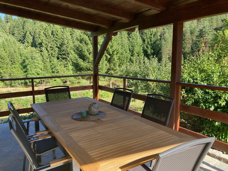 Überdachte Holzterrasse mit Esstisch und Blick auf den Wald